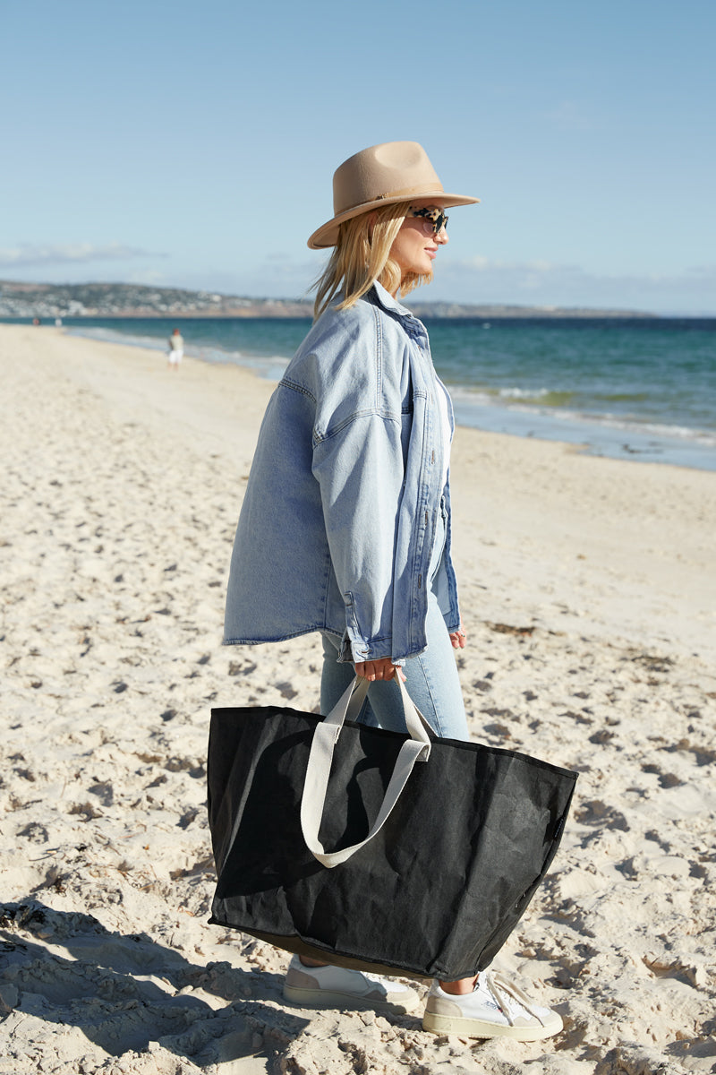 Woman at the beach carrying a large black reusable bag