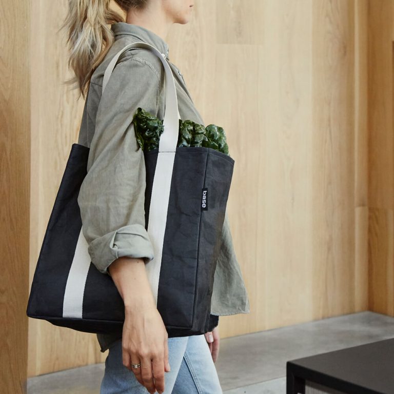 Woman with green shirt carrying black reusable grocery back