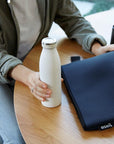 woman on a desk holding white water bottle and neoprene bag